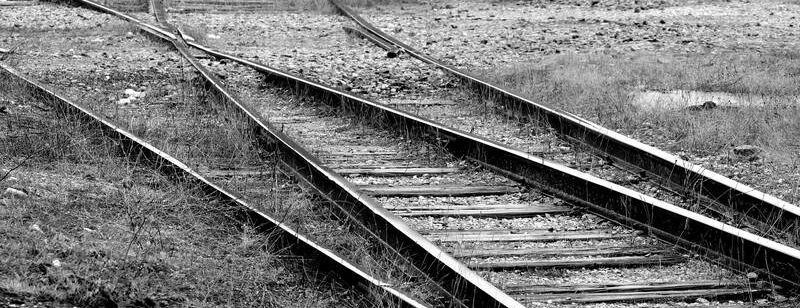 Schwarzweißfoto von Eisenbahnschienen, die in einer kargen, grasbewachsenen Gegend auseinandergehen.